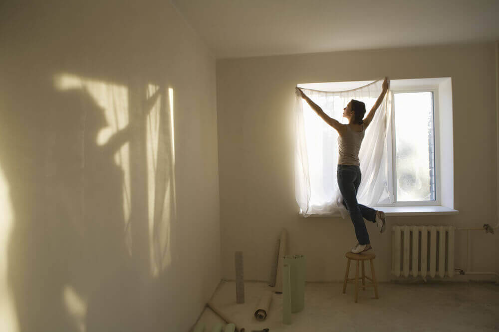 woman hanging up sheer curtain panel