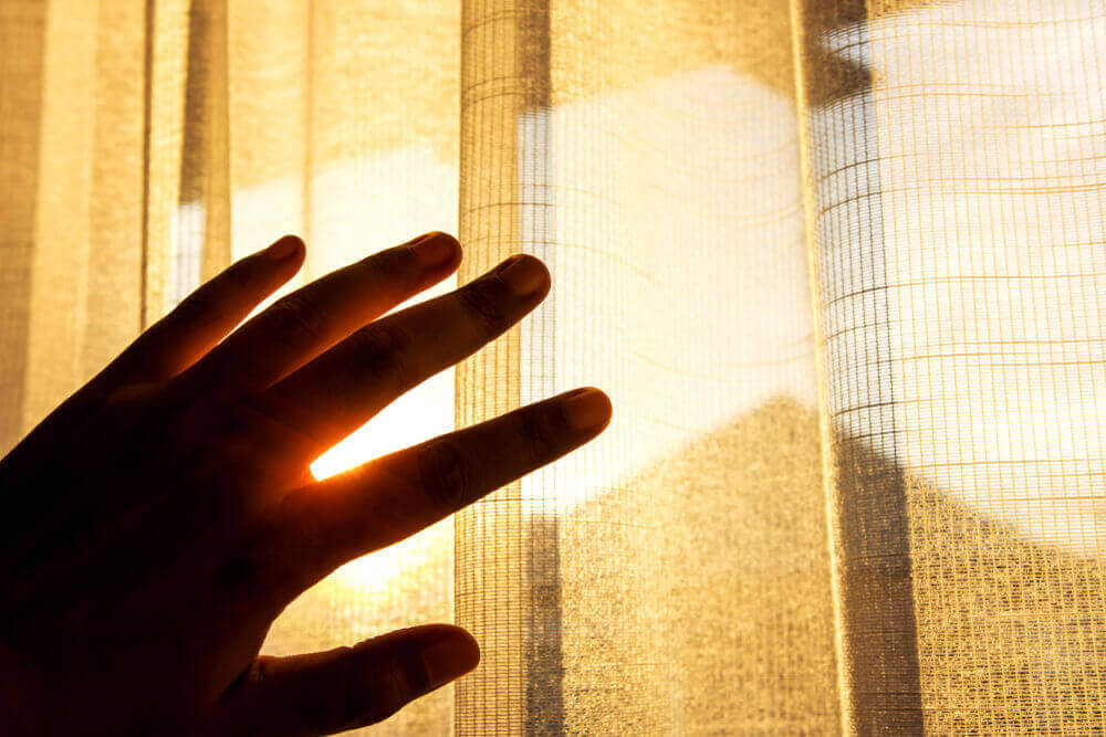 a hand near curtains in the sun